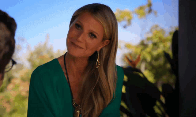 a woman wearing a green top and gold earrings smiles for the camera