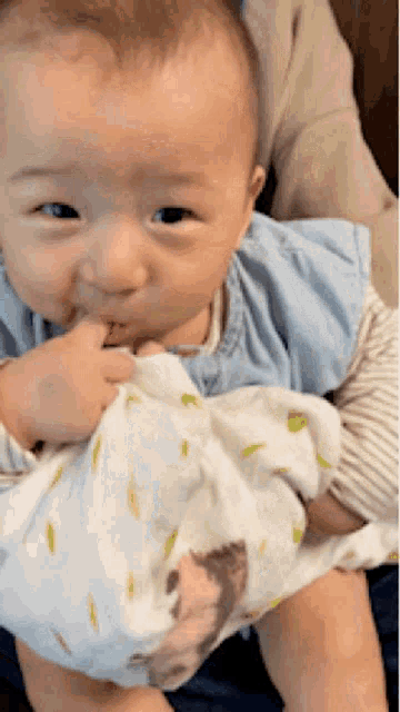 a baby is being held in a person 's arms and licking his fingers