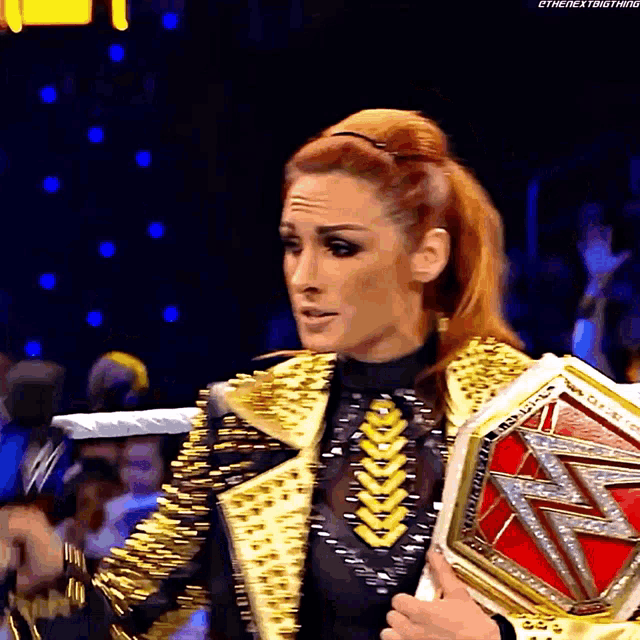 a woman in a gold jacket is holding a wrestling championship
