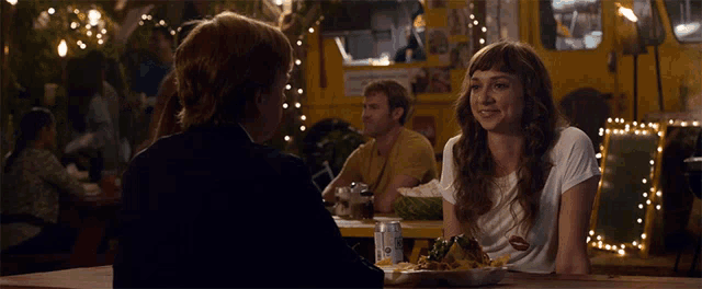 a man and a woman sit at a table in front of a food truck