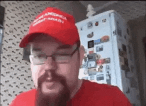 a man with a beard wearing a red hat and glasses is talking on a video call .