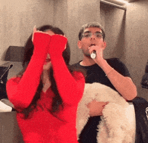 a man is singing into a microphone next to a woman who is covering her eyes with her hands .