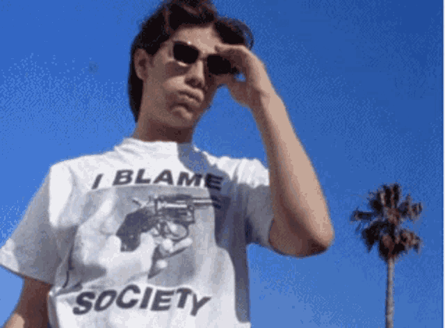 a man wearing sunglasses and a white shirt that says i blame society