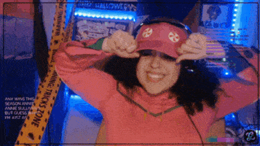 a woman wearing a pink hat and headphones stands in front of a warning tape that says halloween