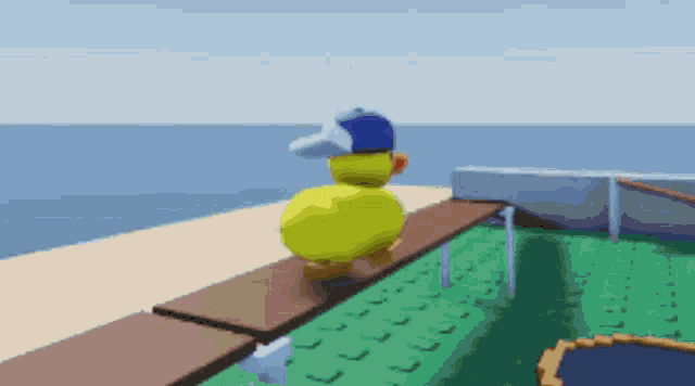 a yellow rubber duck wearing a blue hat is standing on a wooden bench near the ocean .