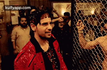 a man in a red jacket is standing in front of a chain link fence in a boxing ring .