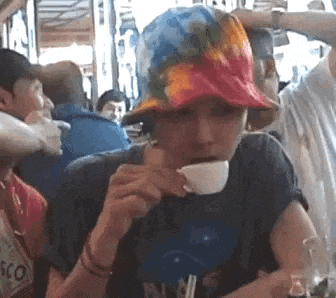 a man wearing a colorful hat is drinking from a cup while sitting at a table .