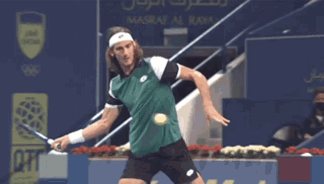 a man in a green shirt and black shorts is swinging a tennis racquet