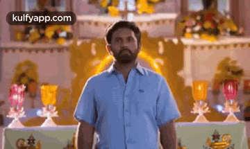 a man in a blue shirt is standing in front of a church with a beard .