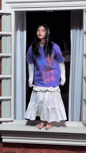 a girl in a purple shirt and white skirt is standing in a window sill