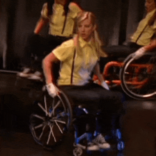 a woman in a yellow shirt and suspenders is sitting in a wheelchair