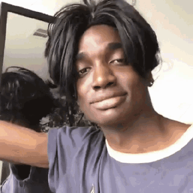 a man wearing a wig and a blue shirt is standing in front of a mirror .