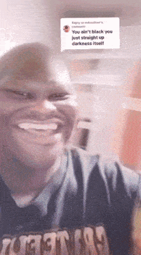 a man wearing a t-shirt that says " you ain t black you just straight up darkness itself " smiles