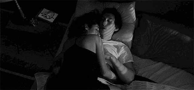 a black and white photo of a man and woman hugging each other while laying on a bed .