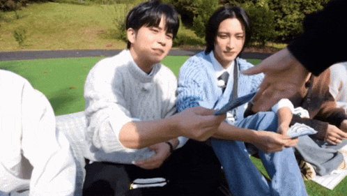a group of young men are sitting on the grass one of them is holding a piece of paper