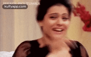 a woman in a black dress is smiling and laughing while sitting on a bed .