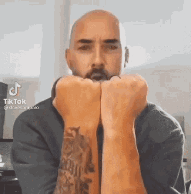 a bald man with a tattoo on his arm is making a funny face with his fists .
