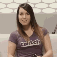 a woman is sitting on a couch wearing a purple t-shirt with the word twitch on it .