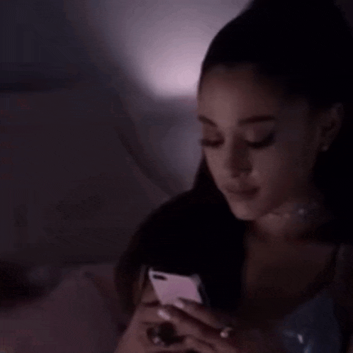 ariana grande is looking at her phone in the dark .