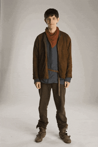 a young man wearing a scarf around his neck is standing in front of a white wall