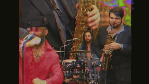 a man in a red shirt is singing into a microphone while a man in a suit plays a saxophone