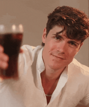 a young man in a white shirt is holding a glass of coke
