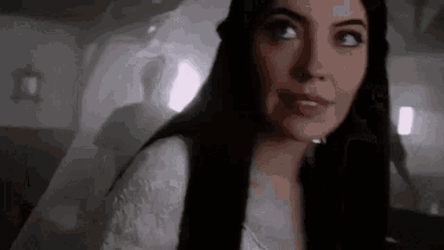 a woman with long black hair is standing in a dark room .