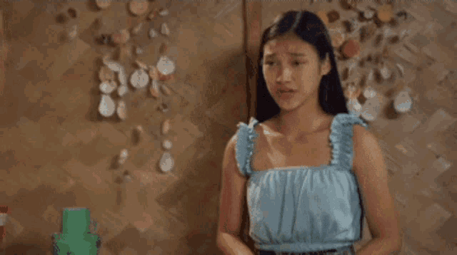 a woman in a blue top is standing in front of a wall with seashells hanging from it .