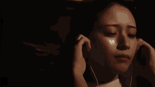 a woman with tears on her face is listening to music with earbuds