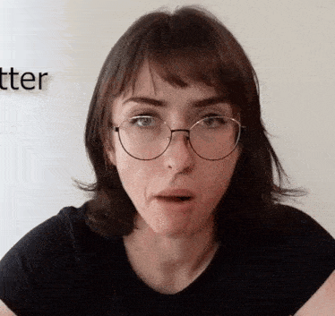 a woman wearing glasses and a black shirt with the word tter on the wall behind her