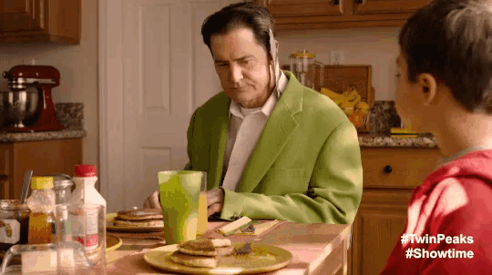 a man in a green suit is sitting at a table with pancakes and a child .