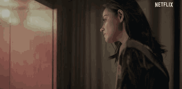 a woman looking out a window with a netflix logo on the bottom