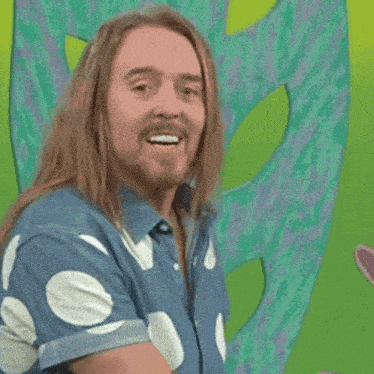 a man with long hair and a beard is smiling in front of a green background that says " i practise every day "