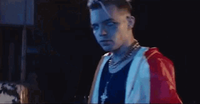 a young man wearing a red , white and blue jacket and a necklace is standing in front of a black background .