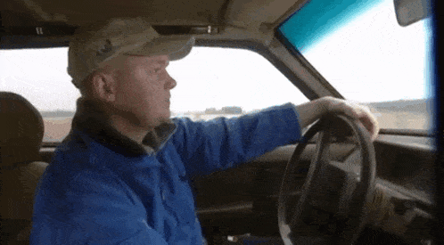 a man in a blue jacket is driving a car while wearing a hat with the letter a on it
