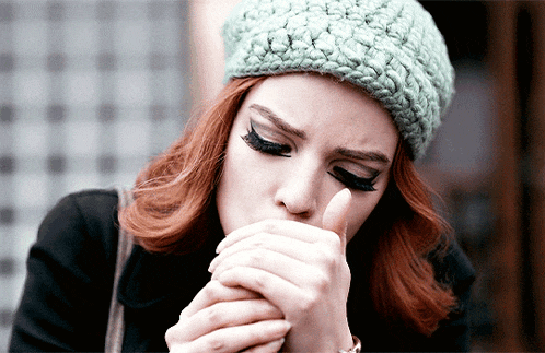 a woman with red hair wearing a green knitted hat is coughing