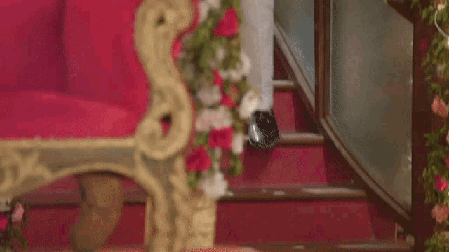 a man in a red suit is standing in front of a couch with flowers on it .
