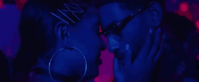 a man and a woman are kissing in a dark room . the woman is wearing hoop earrings .