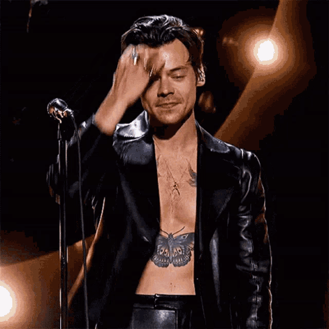 a man with a tattoo of a butterfly on his chest is singing into a microphone .