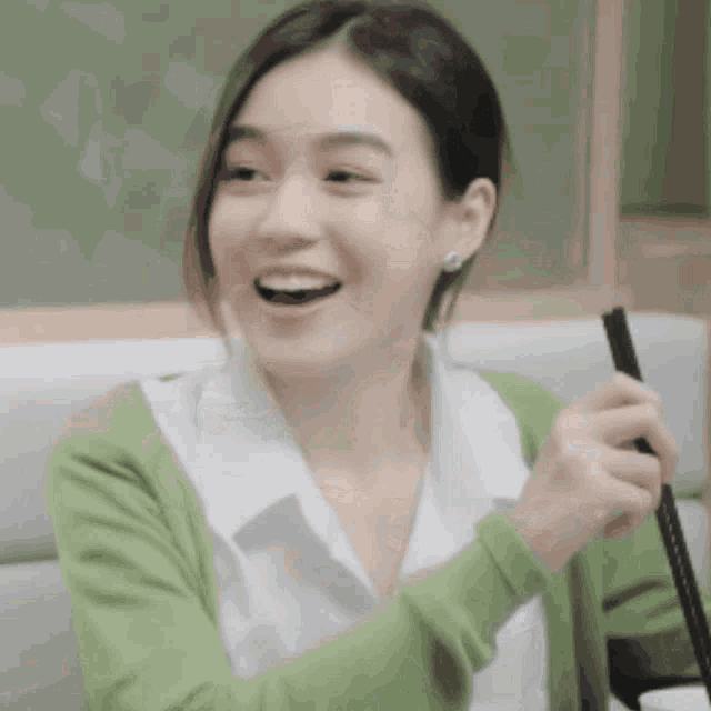 a woman wearing a green sweater is holding chopsticks and smiling