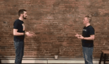 two men are standing in front of a brick wall and talking to each other with the words what no omg written above them