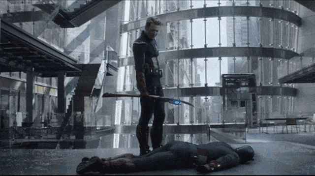 a man standing next to a man laying on the floor holding a sword .