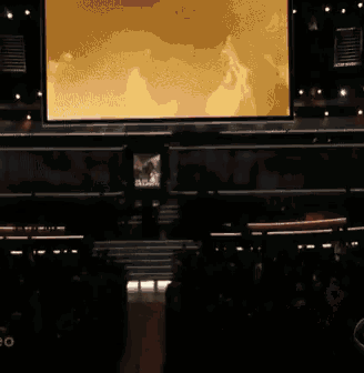 a large screen in a dark room shows a picture of a man standing in front of a fire