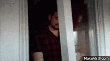 a man in a plaid shirt is standing in a doorway looking out a window .