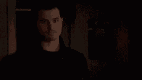 a man in a black jacket is standing in a dark room and looking at the camera .
