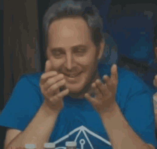 a man wearing a blue shirt is covering his face with his hand .