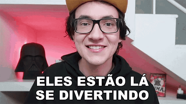 a man wearing glasses and a hat is smiling with the words eles estao la se divertindo behind him