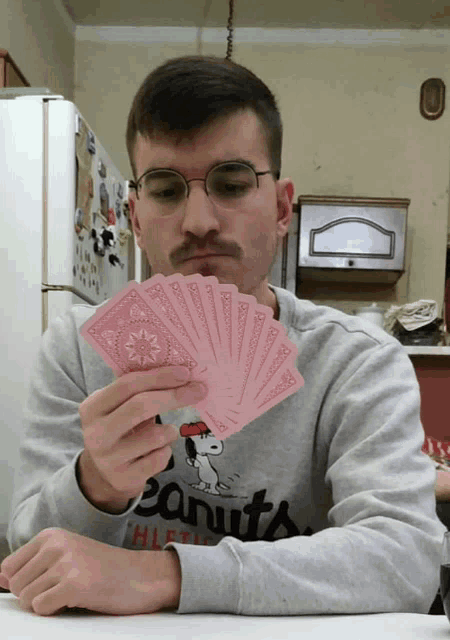 a man wearing a peanuts sweatshirt holds a bunch of pink playing cards