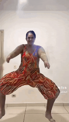 a woman in a red dress is dancing on a tiled floor in a room .