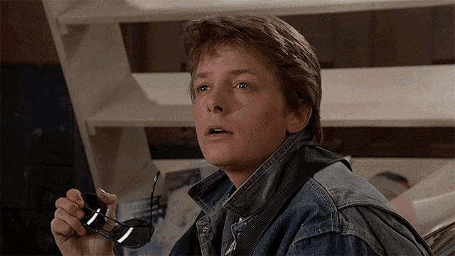 a man in a denim jacket is holding a pair of glasses